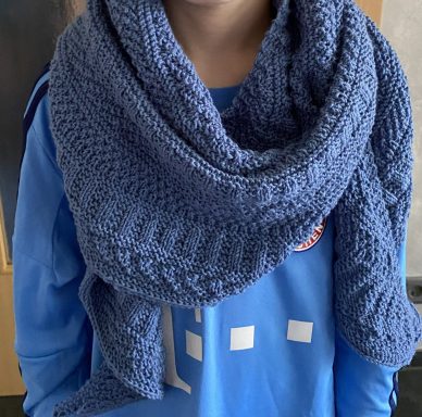 Kind trägt einen blauen, gehäkelten Schal über einem blauen Sweatshirt.