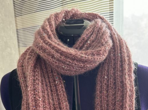Rosa gestrickter Schal mit glitzernden Fäden auf einer Kleiderpuppe.