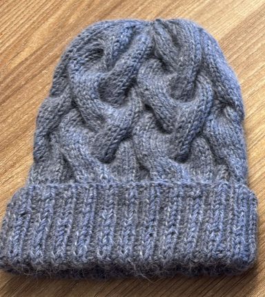 Grau gestrickte Mütze mit Zopfmuster und breitem Bündchen.