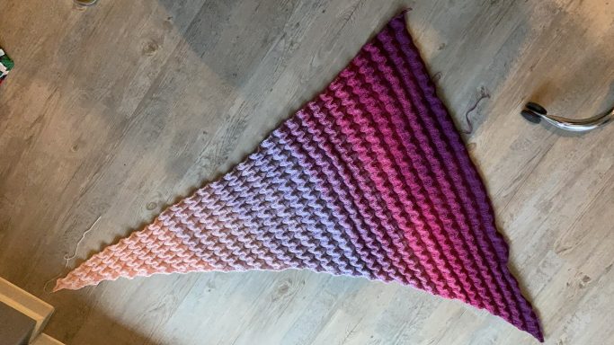 Dreieckiger Stoff in Farbverlauf von Lila zu Orange auf einem hellen Boden.