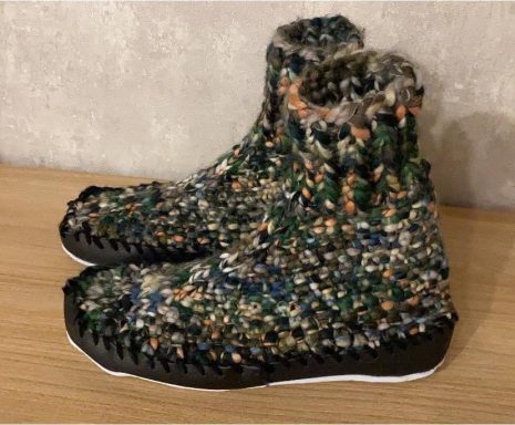 Bunte, gestrickte Hausschuhe mit schwarzer Sohle auf einem Holzuntergrund.