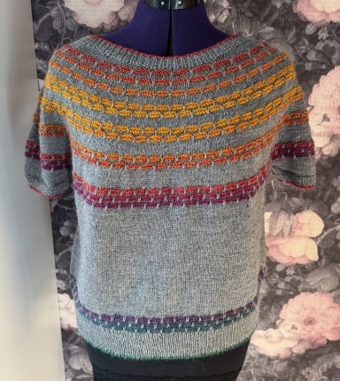 Grauer Pullover mit bunten geometrischen Mustern in Orange, Gelb und Lila.
