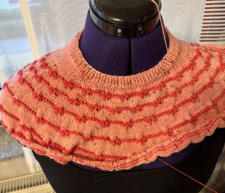 Geflochtene rosa Strickarbeit mit wellenförmigem Muster auf einem Maßanzug.