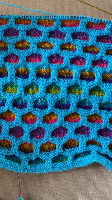 Bunt gemusterte Häkelarbeit in Blau, Lila und Orange mit kreisförmigen Spitzen.