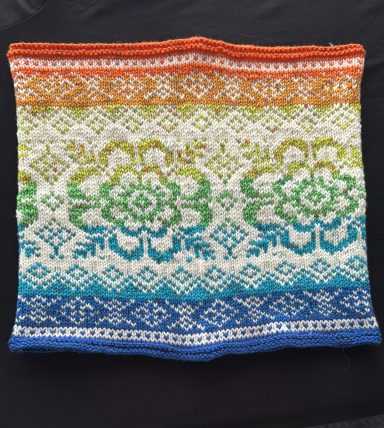 Bunte gestrickte Decke mit floralen und geometrischen Mustern in Regenbogenfarben.