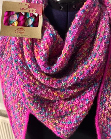 Bunter, gestrickter Schal in Pinktönen, präsentiert auf einem Kleiderbügel.