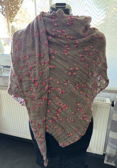 Beige Schal mit roten Blütenmotiven, drapiert auf einer schwarzen Stange.