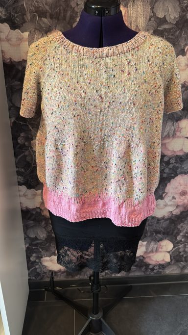 Beige Strickoberteil mit buntem Muster und pinkem Saum, auf einer Schneiderpuppe präsentiert.