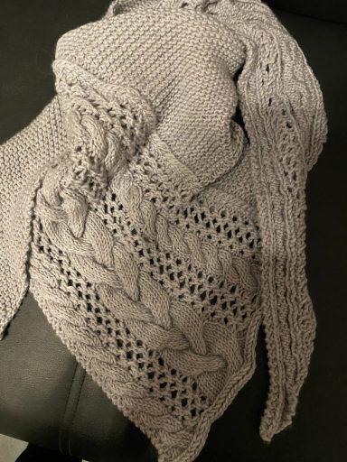 Dunkelgrauer, gestrickter Schal mit Zopfmuster und offenen Maschen.